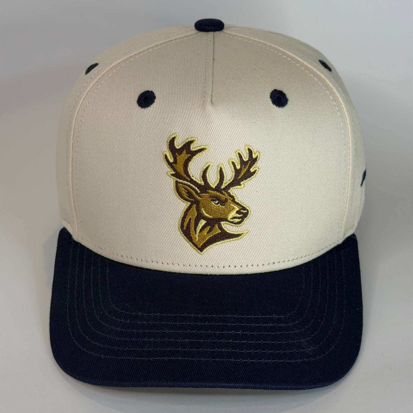 Beige and navy cap with a gold deer logo on a white background