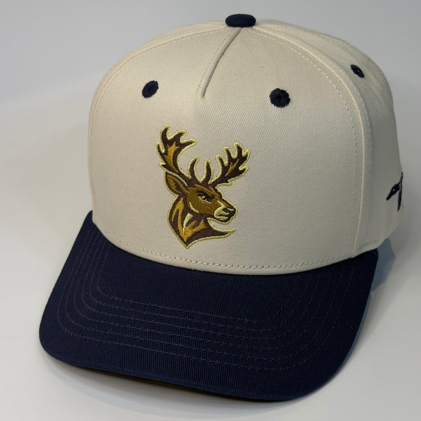 Beige and navy cap with a gold deer logo on a white background