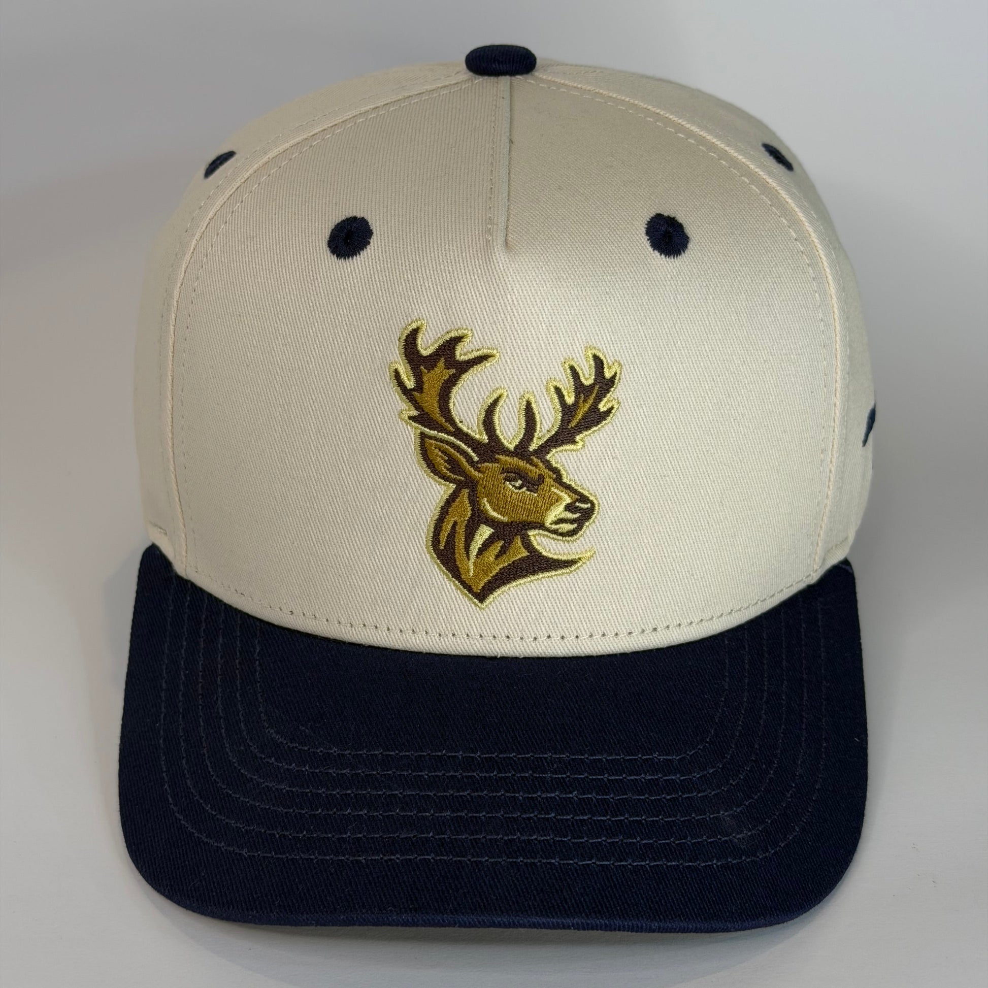 Beige and navy cap with a gold deer logo on a white background