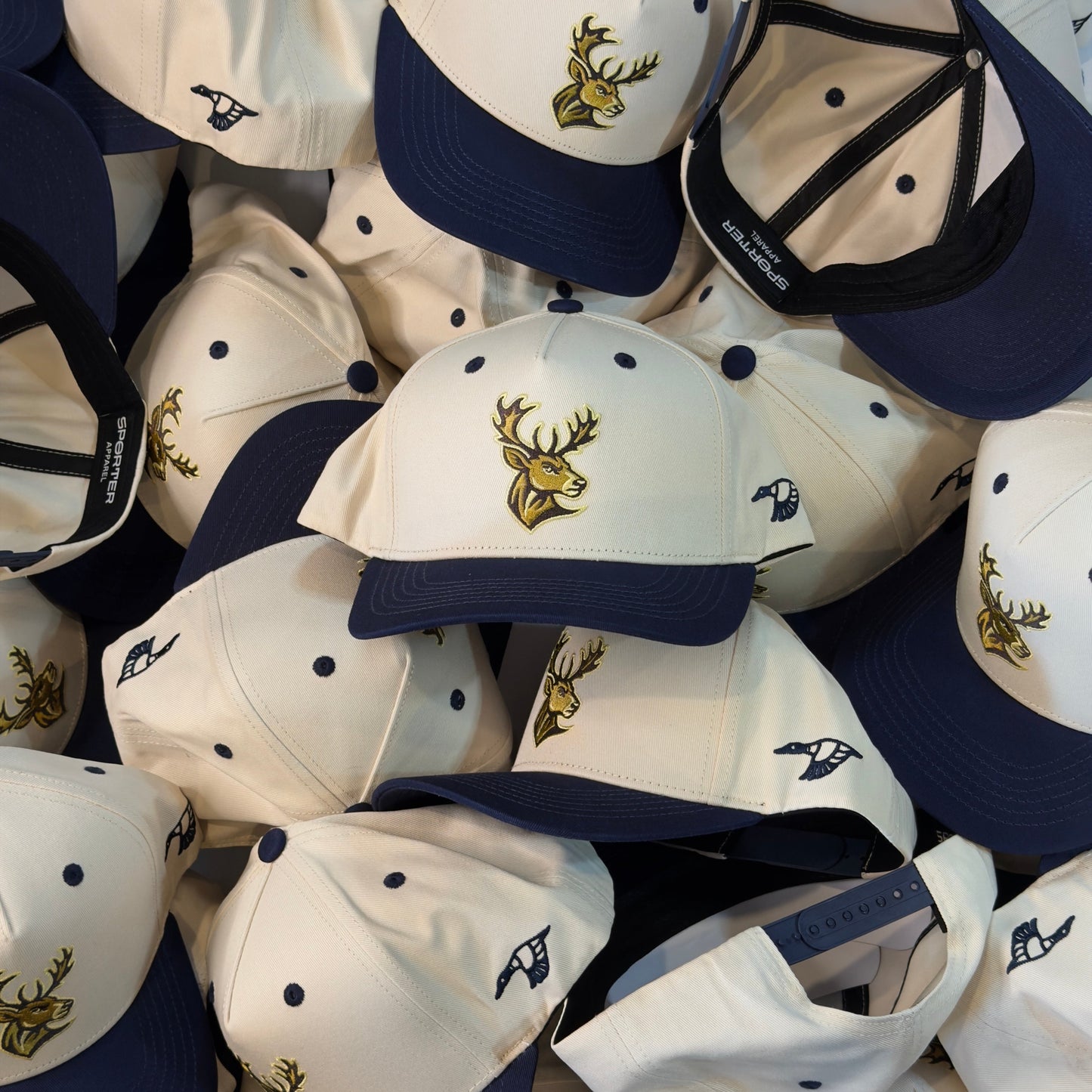 Collection of white and navy baseball caps with a deer logo on a blue background
