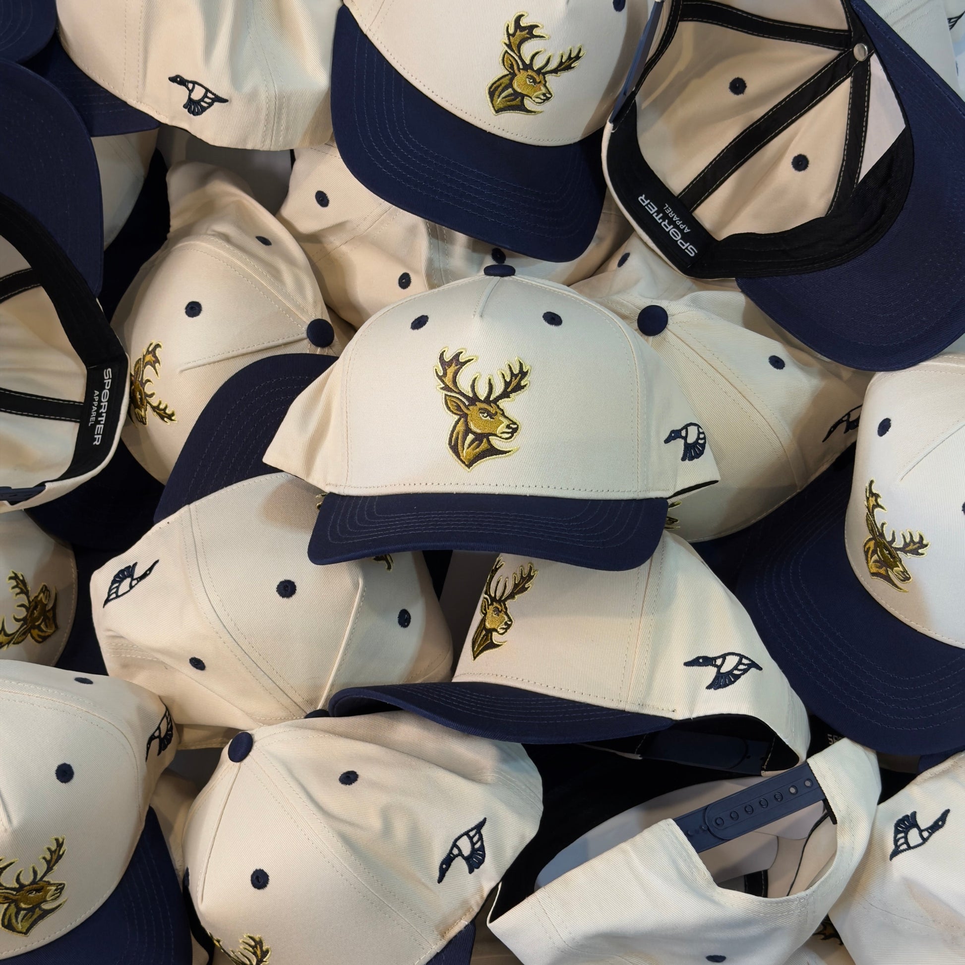 Collection of white and navy baseball caps with a deer logo on a blue background
