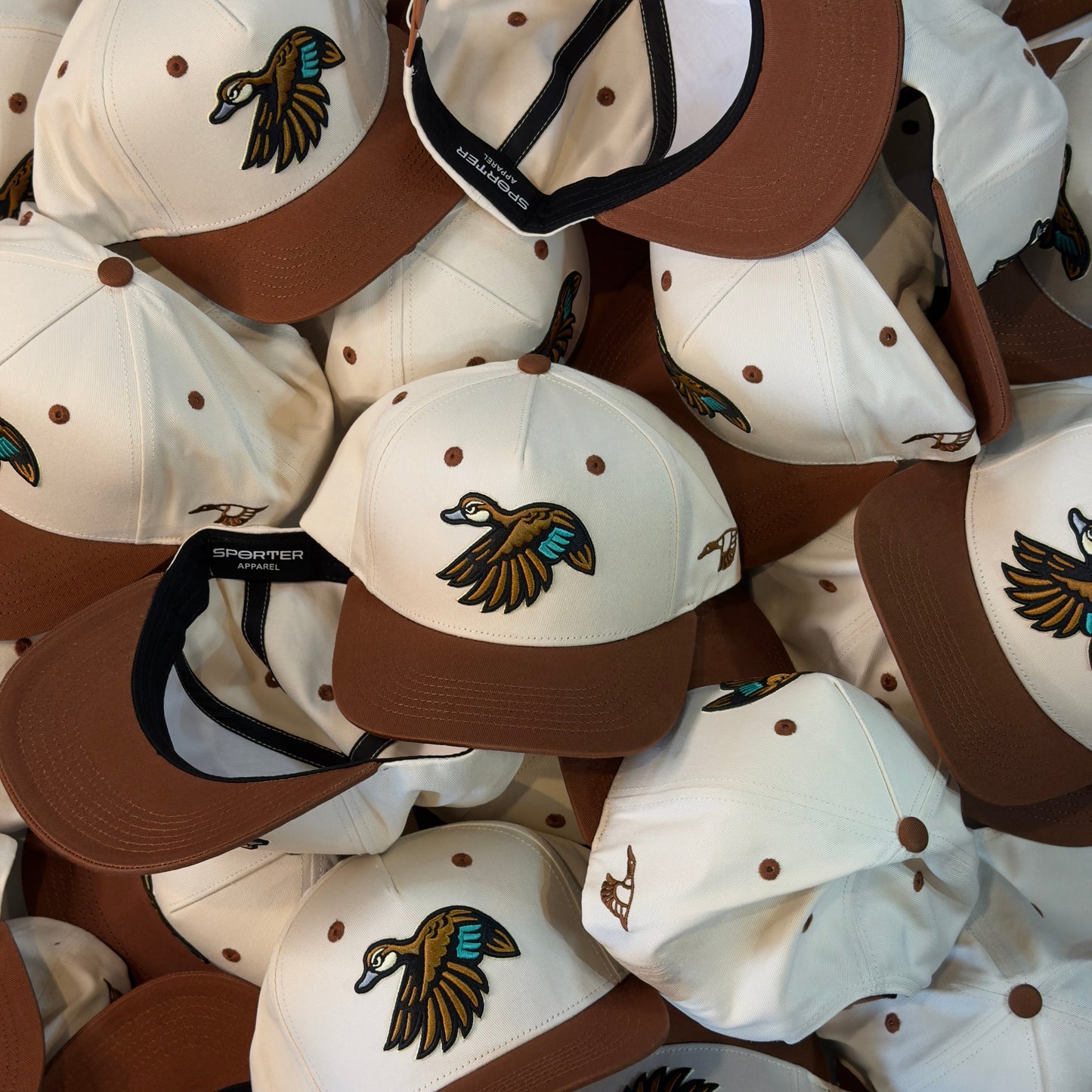 Stack of brown and white caps with a duck logo on a brown background